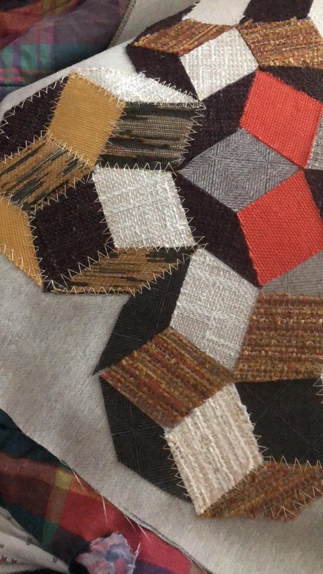 A close-up of zigzag stitches joining textured cream, rust and charcoal fabric